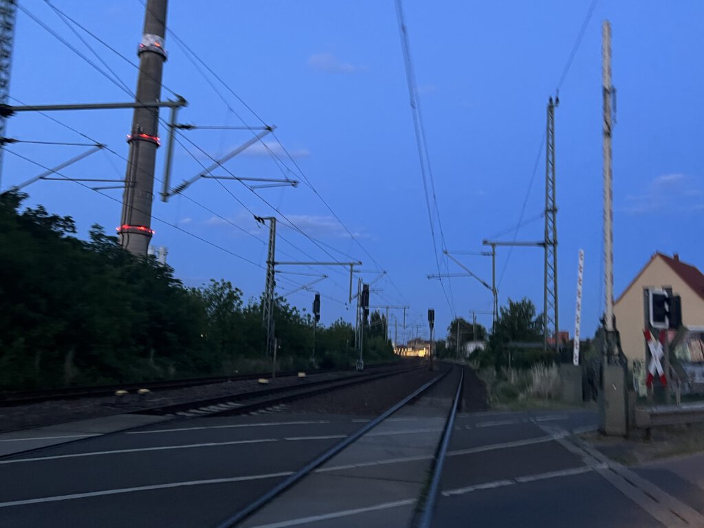 Werder (Havel): Blick vom Bahnübergang auf den beleuchteten Bahnhof am Abend