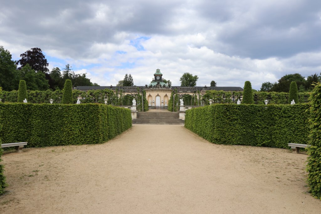 Bildergalerie im Park Sanssouci in Potsdam: Blick über den mit Hecken gesäumten Weg auf die Gartenseite