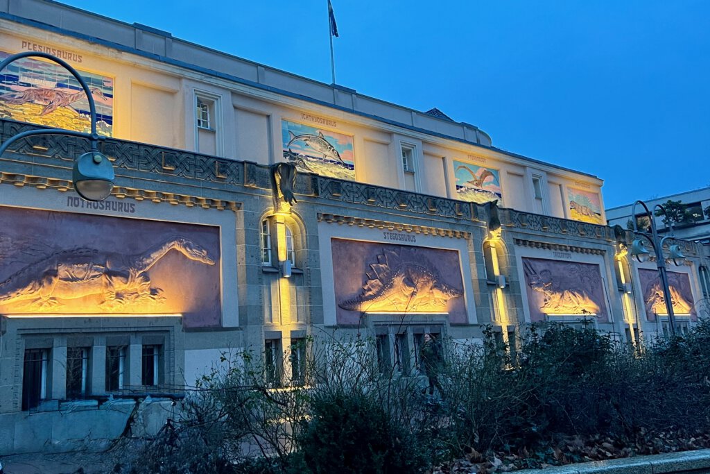 Die beleuchtete Fassade des Aquariums Berlin, am Abend von der Budapester Straße aus fotografiert. Du siehst Tiere aus der Urzeit