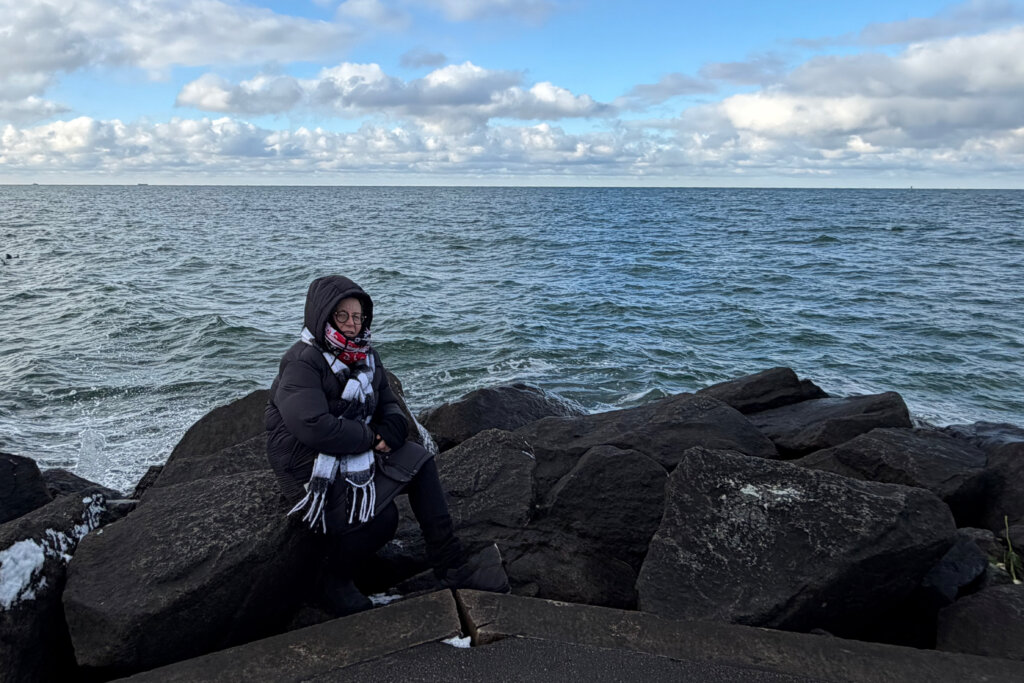 Warnemünde im Winter: Frau dick eingemummelt während einer kurzen Rast auf der Mole.