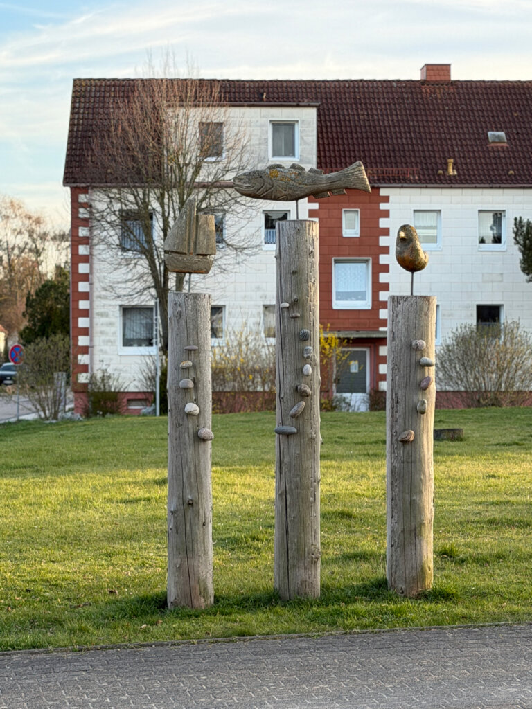 Maritime Holzskulptur mit Fischmotiv in Kirchdorf auf der Insel Poel vor Wohnhäusern und Wiese